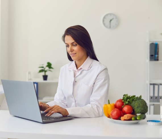 Nutrition Department 1 A nutritionist at Levantine Medical Center creating a personalized meal plan on a laptop with fresh fruits and vegetables on the table